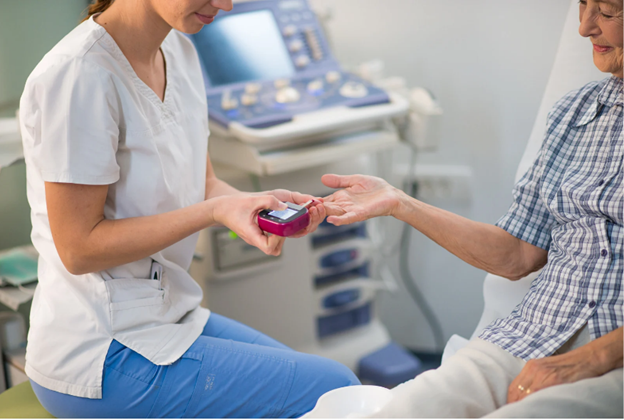 The image shows a healthcare professional, likely a nurse, assisting an elderly individual with a medical device while standing in a hospital room.