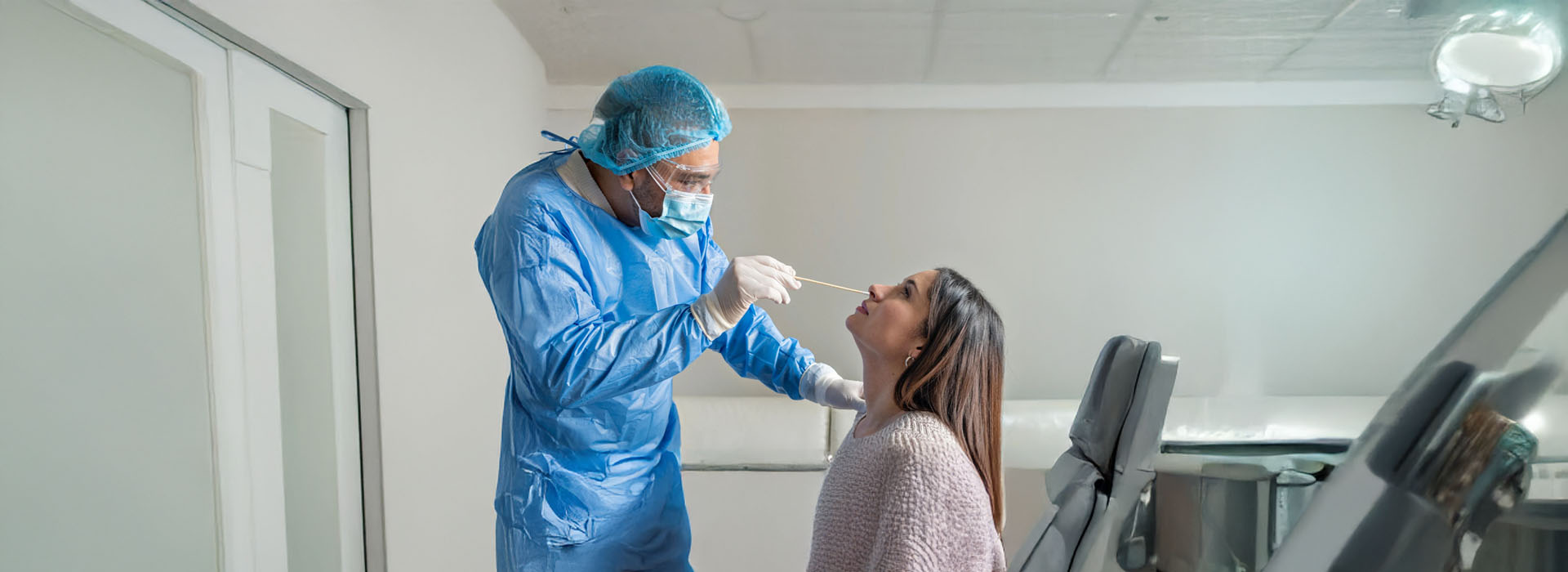 The image shows a medical professional in blue scrubs performing a procedure on a patient lying down, with a syringe being used, all within a clinical setting.