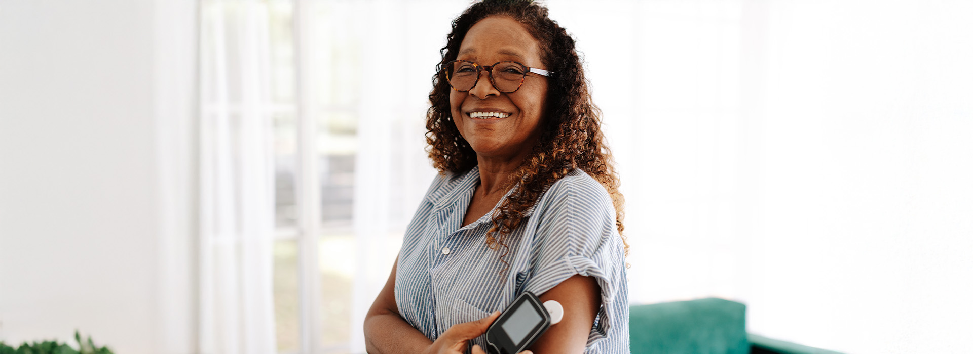 The image shows a woman with glasses sitting at a table, smiling and looking directly at the camera.