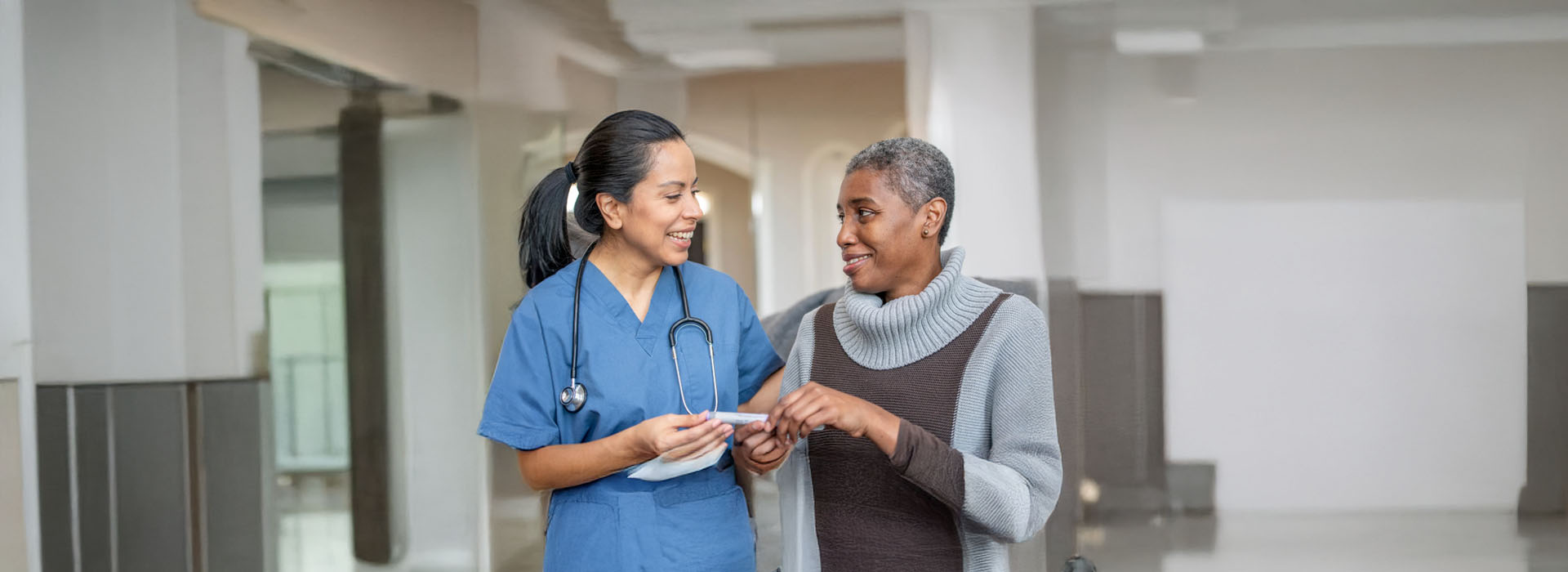 The image shows two individuals in a hospital setting  one appears to be a medical professional assisting another person who might be a patient, with both engaged in an interaction involving a piece of paper.