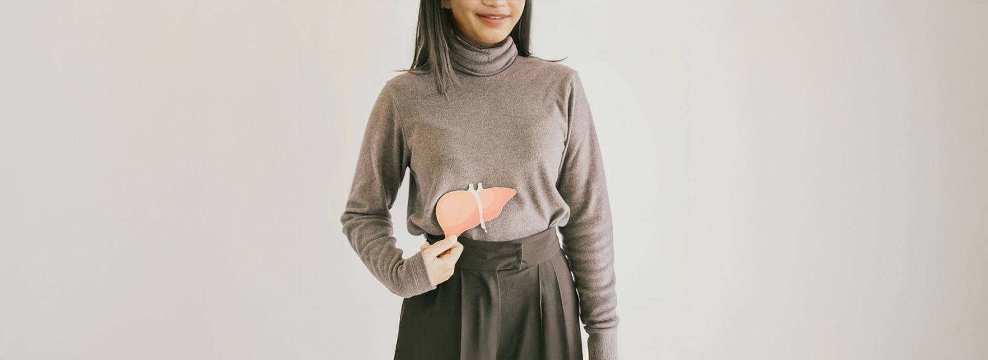 A person wearing a dark top stands against a white background with a blurred foreground.