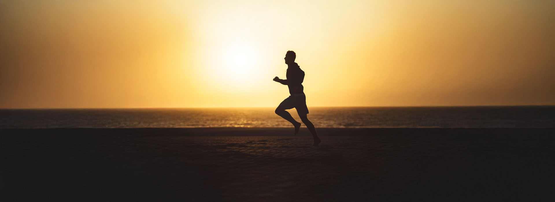 A person running along a beach at sunset with an orange sky in the background.