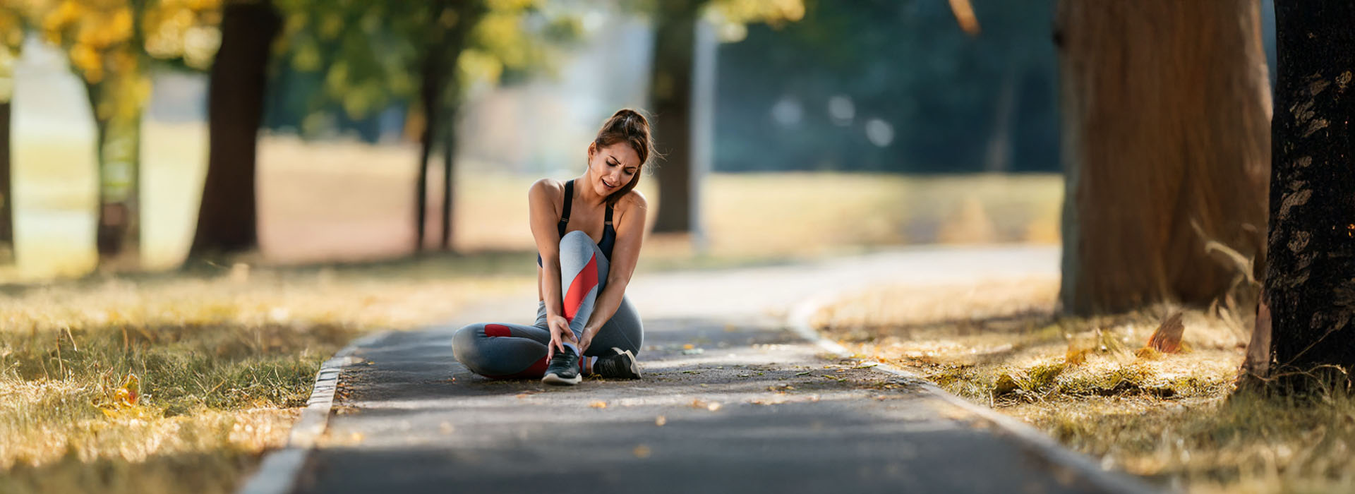 A woman stretching on a pathway with trees in the background.