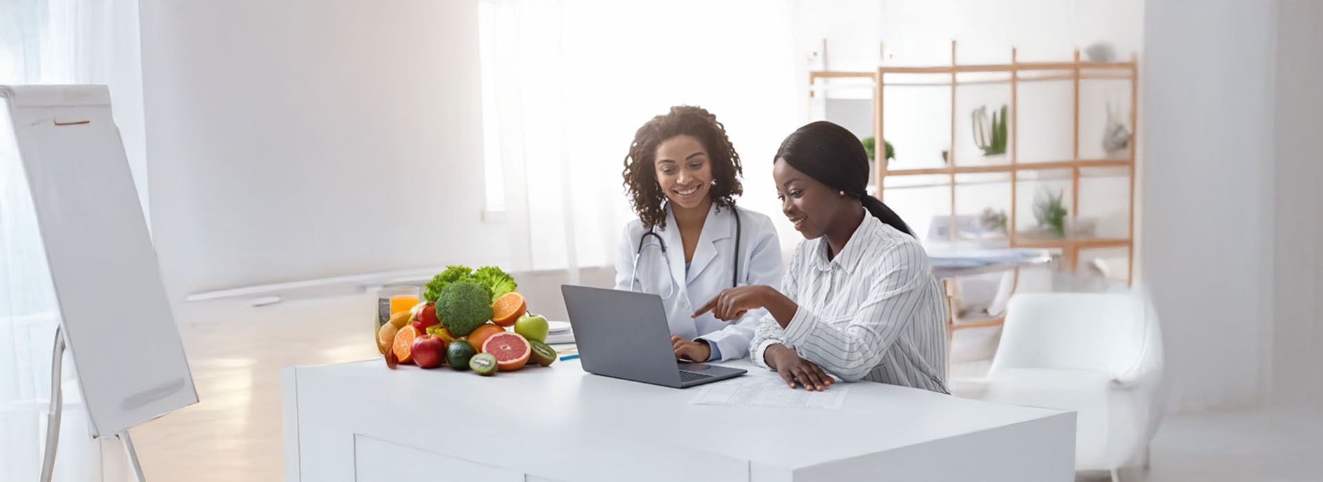 A photograph captures two individuals seated at a table with laptops, engaged in conversation, amidst an indoor setting with a modern aesthetic  one person appears to be gesturing while speaking.