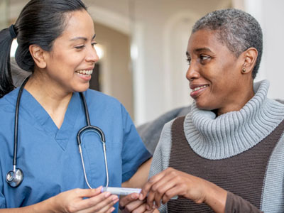 Two individuals, one a woman wearing a stethoscope around her neck and the other an older adult, are engaged in a conversation with each other.