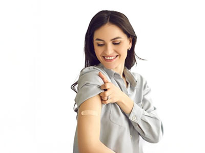 A woman with light skin smiling at the camera while pointing to her arm where she has received a COVID-19 vaccine shot.