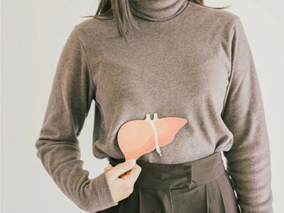 A person wearing a gray sweater and holding an orange object that resembles a heart over their stomach.