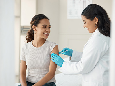 The image shows a medical professional administering a COVID-19 vaccine to a patient in a clinical setting.