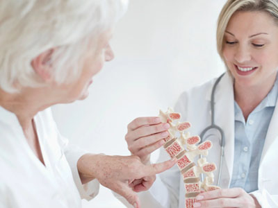 The image features two elderly individuals sitting with a medical professional, who appears to be a chiropractor, holding an X-ray model of a spine, possibly during a consultation or examination.