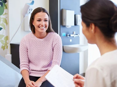 A woman seated at a desk in a medical office, smiling at another woman who is handing her a card.