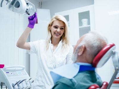 A woman standing next to a man who is sitting in a dental chair, with medical equipment around them, possibly a dentist s office.
