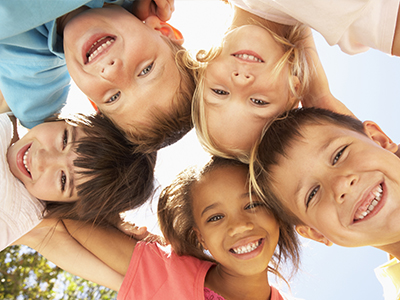 The image depicts a group of children of various ages smiling at the camera from different angles.